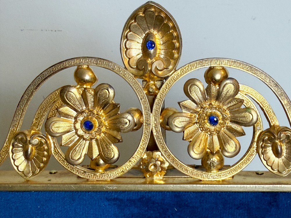 A rectangular gilt bronze picture frame featuring a blue velvet border, ornate corner mounts, and an elaborate floral crest at the top. View VII