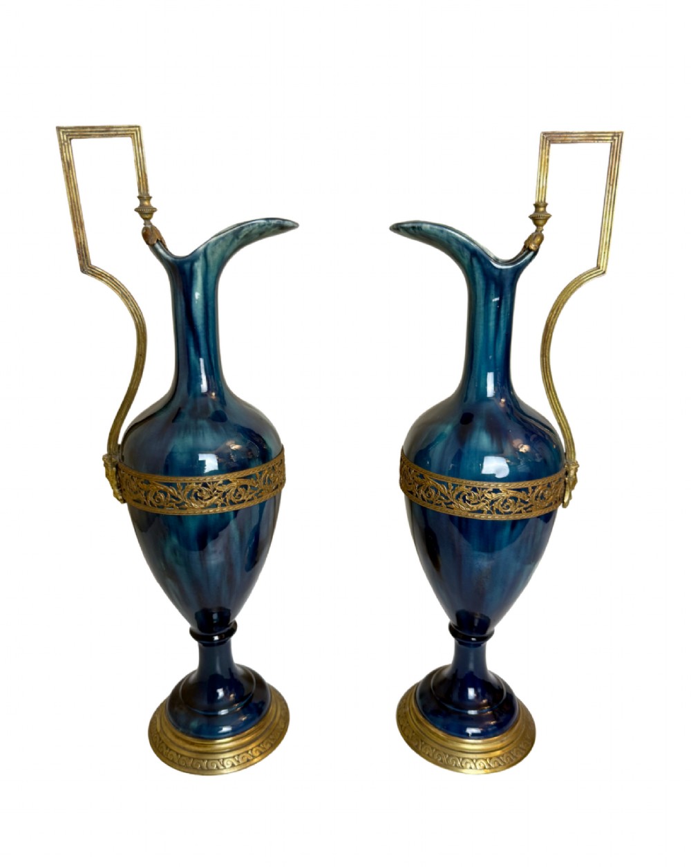 A pair of slender blue porcelain ewers featuring decorative gilt bronze mounts, angular handles, and flared spouts.
