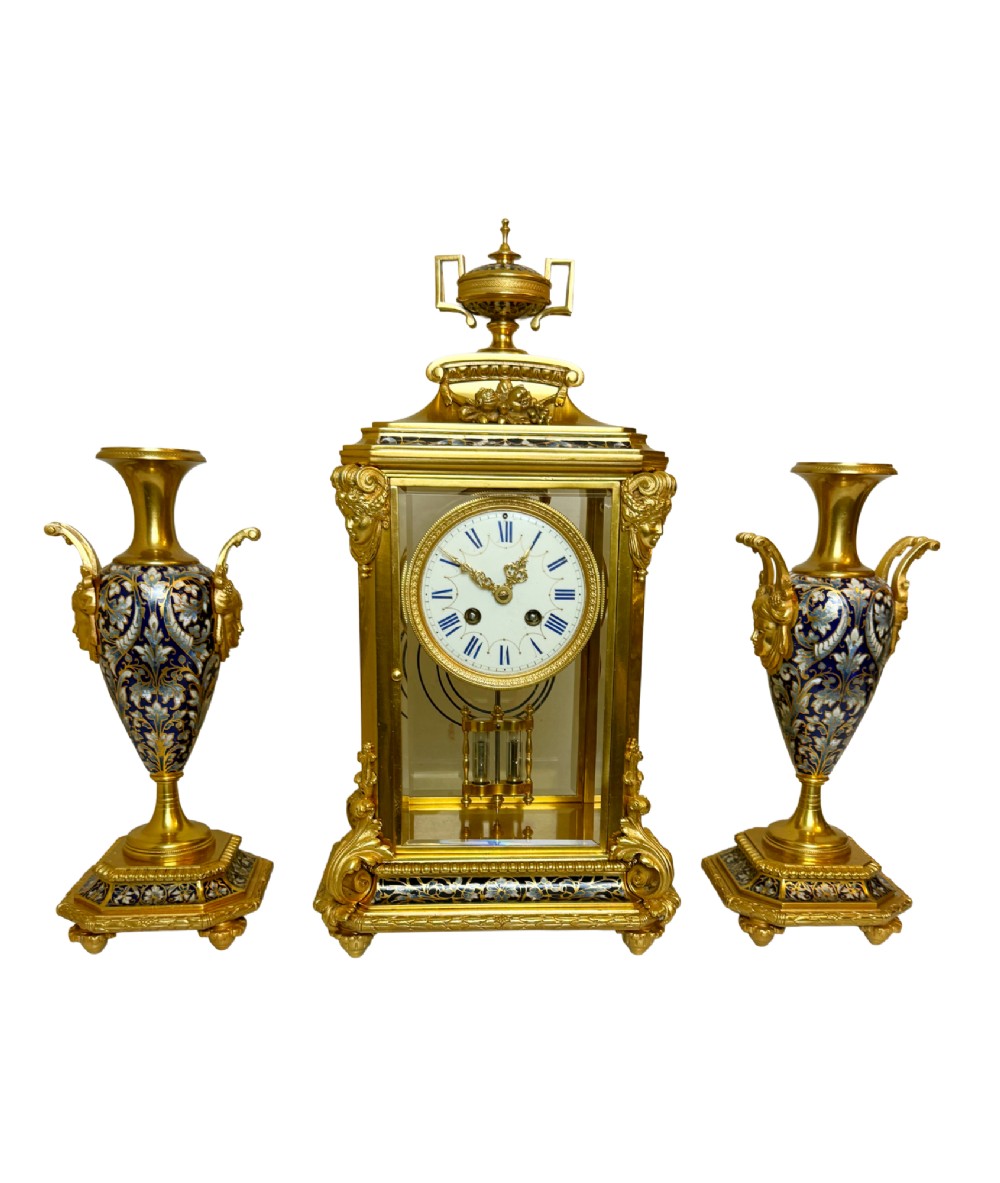 A late 19th-century French clock garniture featuring a gilt bronze mantel clock flanked by two matching champleve enamel side urns.