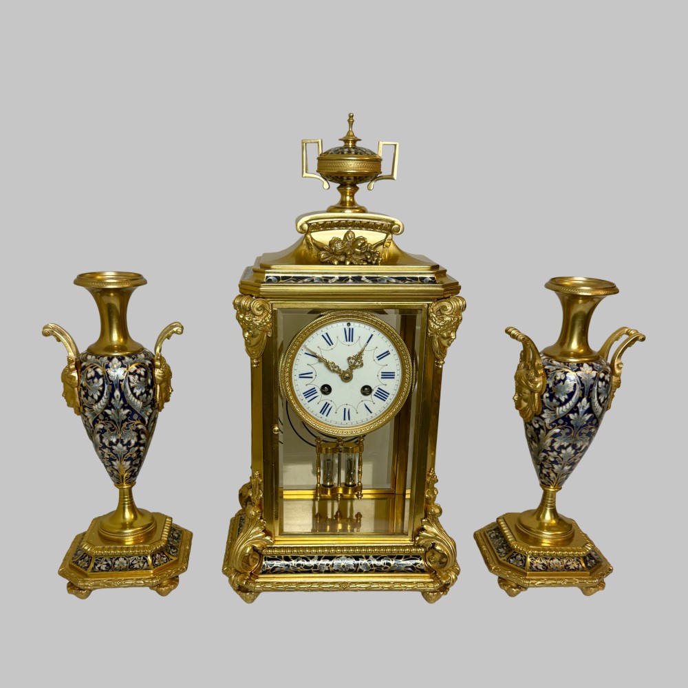 A late 19th-century French clock garniture featuring a gilt bronze mantel clock flanked by two matching champleve enamel side urns. View XIV