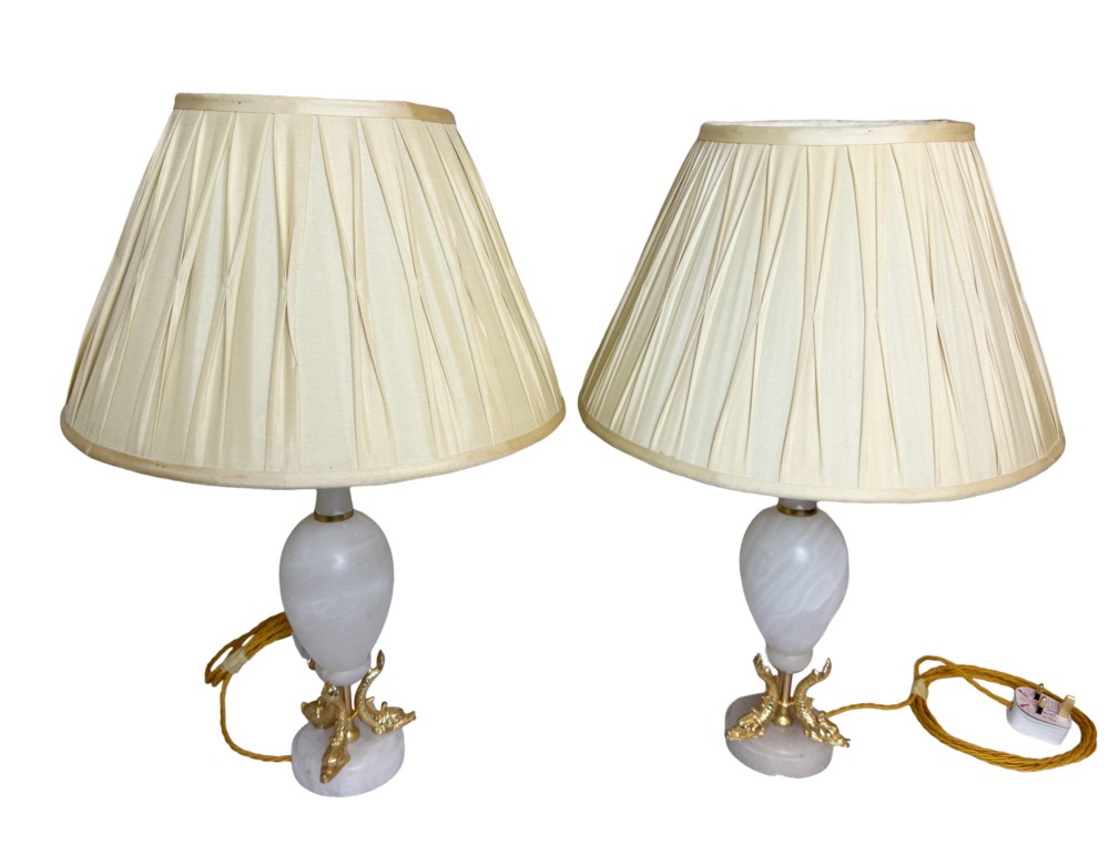 A pair of French onyx urn-shaped table lamps featuring gilt bronze dolphin feet and cream pleated shades.