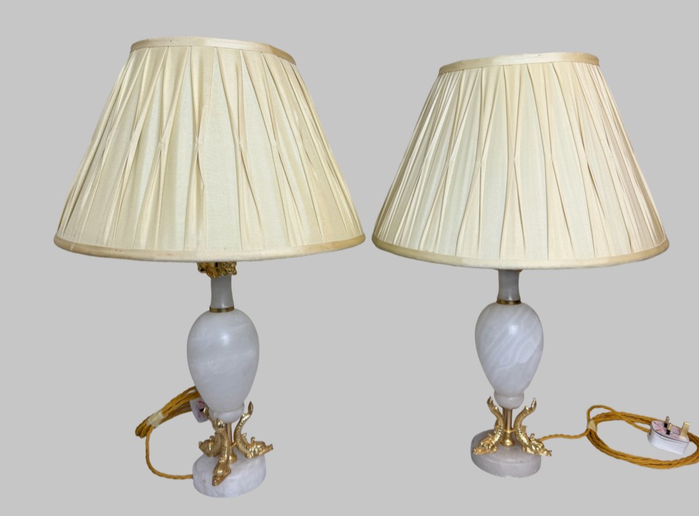 A pair of French onyx urn-shaped table lamps featuring gilt bronze dolphin feet and cream pleated shades. View VII