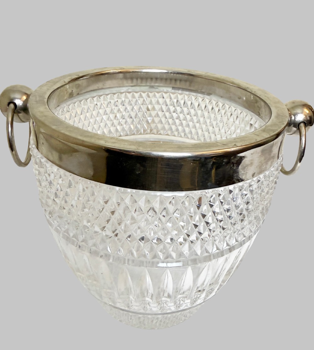 A French circa 1920 clear cut crystal ice bucket featuring geometric diamond facet cuts, a silver-plated rim, and round drop-ring side handles. View II