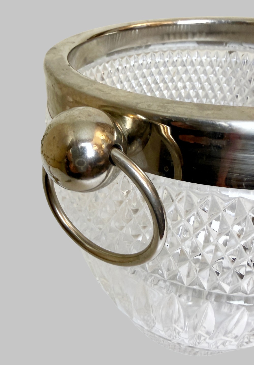 A French circa 1920 clear cut crystal ice bucket featuring geometric diamond facet cuts, a silver-plated rim, and round drop-ring side handles. View III