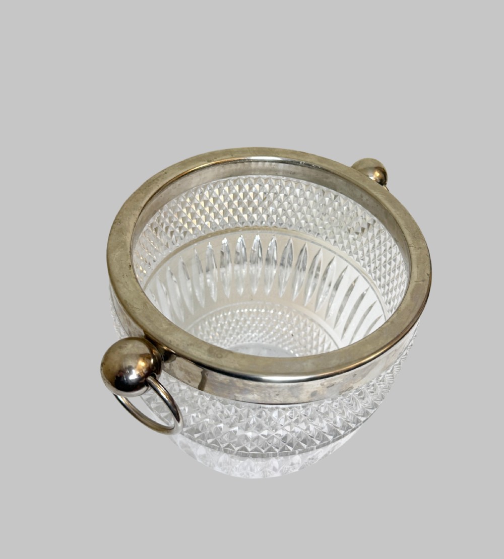 A French circa 1920 clear cut crystal ice bucket featuring geometric diamond facet cuts, a silver-plated rim, and round drop-ring side handles. View IV