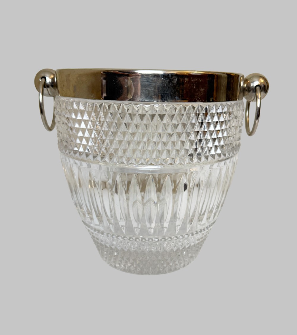 A French circa 1920 clear cut crystal ice bucket featuring geometric diamond facet cuts, a silver-plated rim, and round drop-ring side handles. View VI