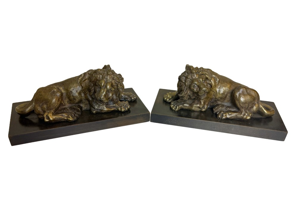 A pair of late 19th-century patinated bronze sculptures depicting recumbent lions resting on dark rectangular marble bases.