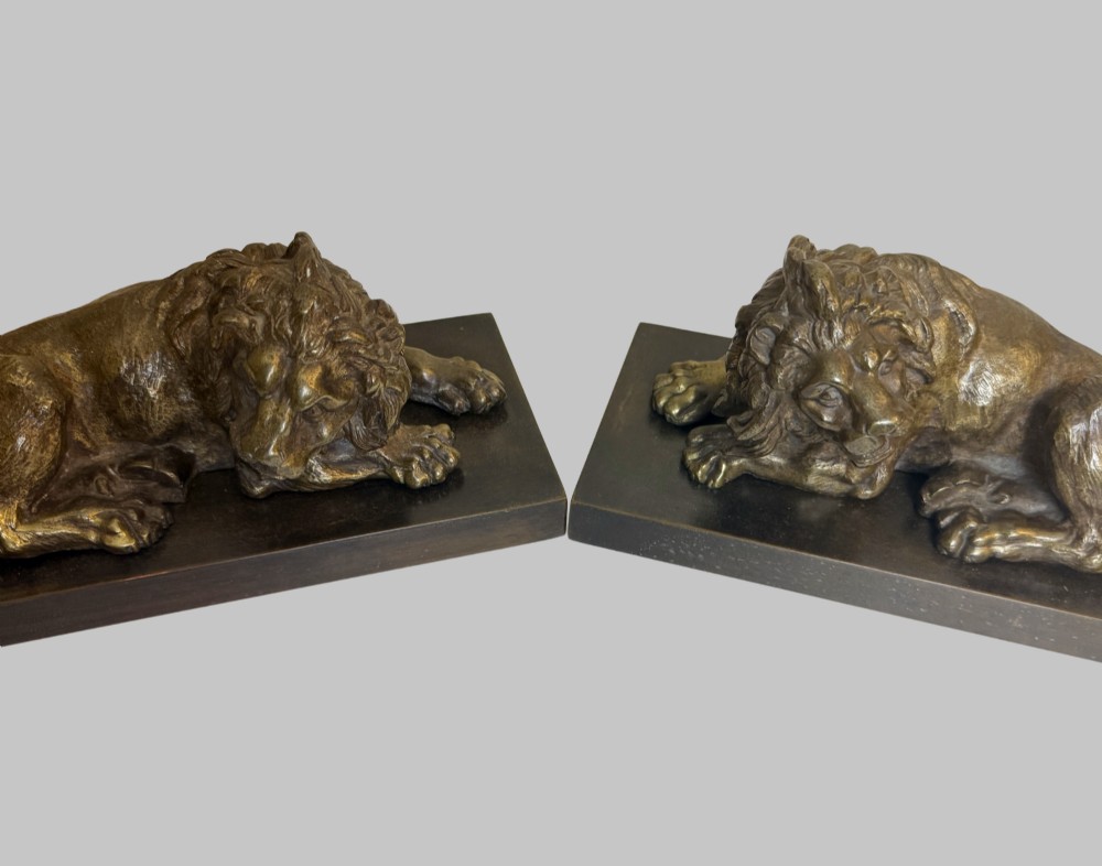 A pair of late 19th-century patinated bronze sculptures depicting recumbent lions resting on dark rectangular marble bases. View II