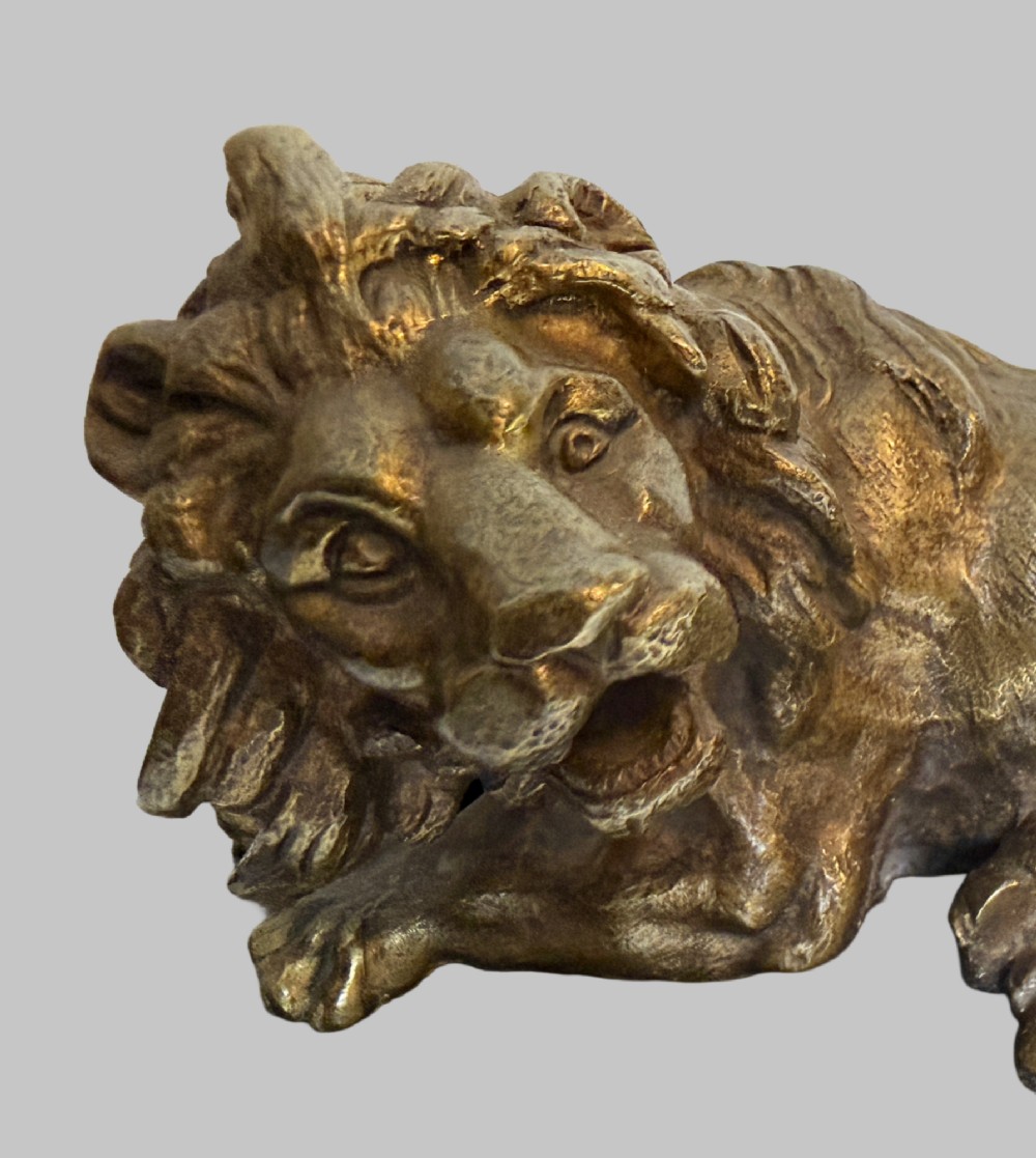 A pair of late 19th-century patinated bronze sculptures depicting recumbent lions resting on dark rectangular marble bases. View VI