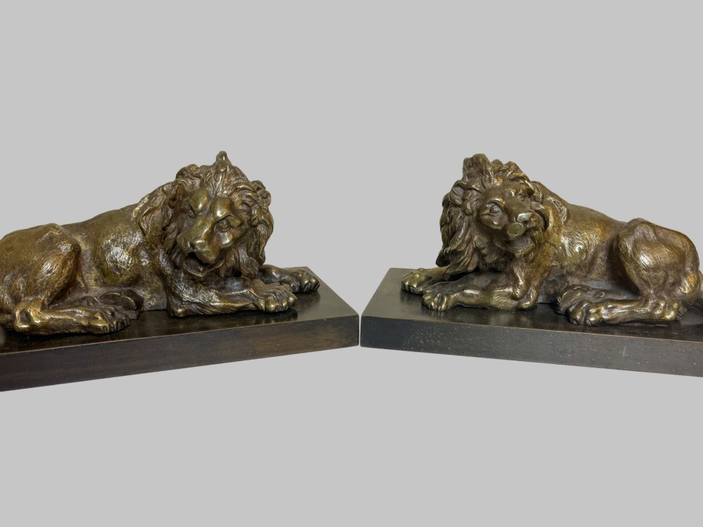 A pair of late 19th-century patinated bronze sculptures depicting recumbent lions resting on dark rectangular marble bases. View VII