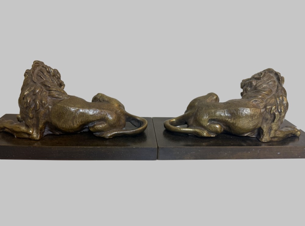A pair of late 19th-century patinated bronze sculptures depicting recumbent lions resting on dark rectangular marble bases. View VIII