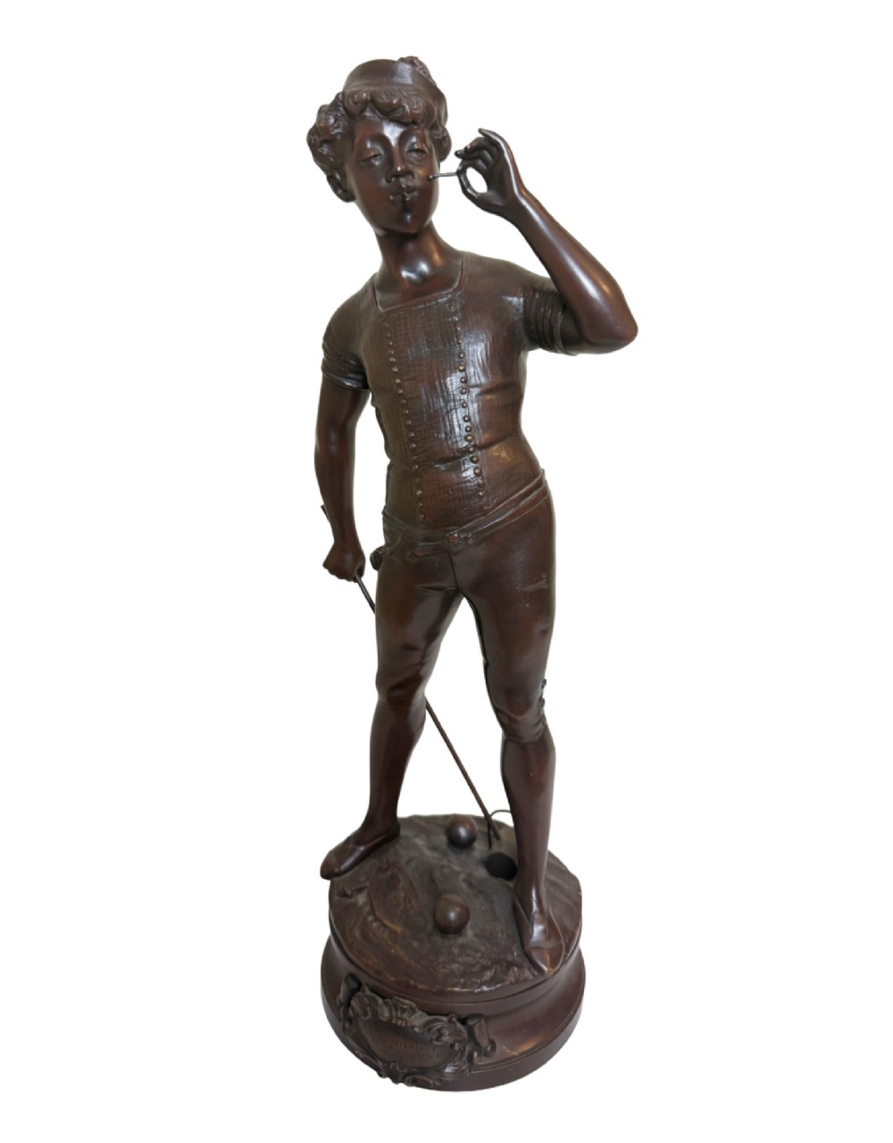 A dark patinated bronze statue of a young man smoking a cigarette while holding a croquet mallet on a round base with croquet balls.