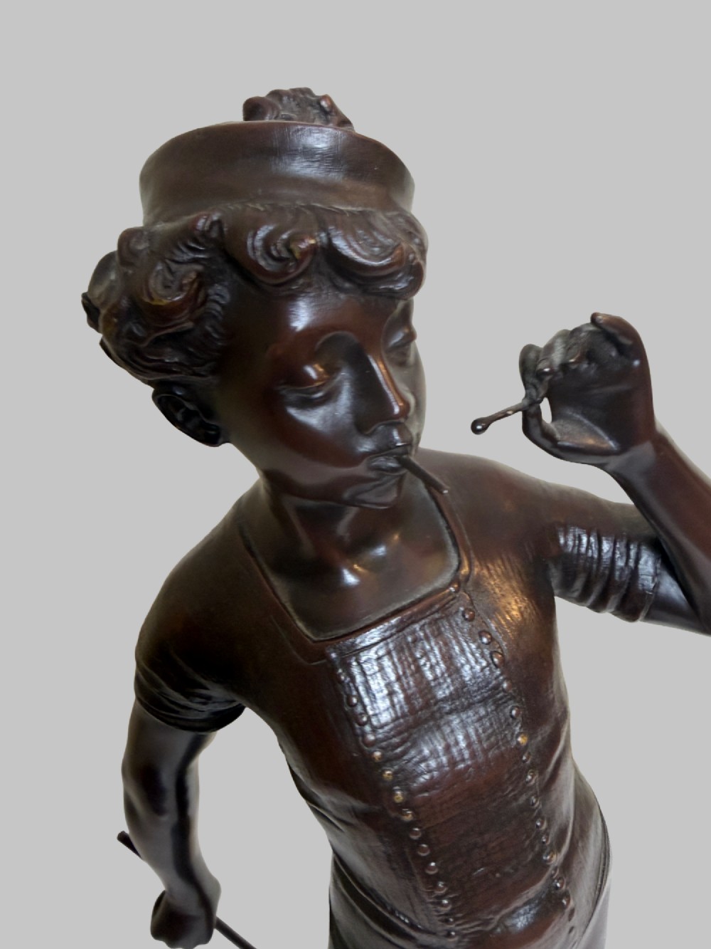 A dark patinated bronze statue of a young man smoking a cigarette while holding a croquet mallet on a round base with croquet balls. View VI