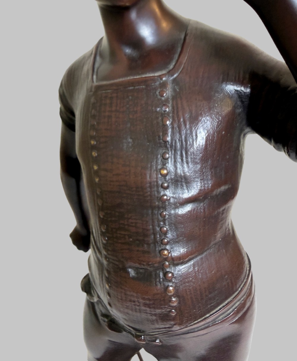 A dark patinated bronze statue of a young man smoking a cigarette while holding a croquet mallet on a round base with croquet balls. View VII