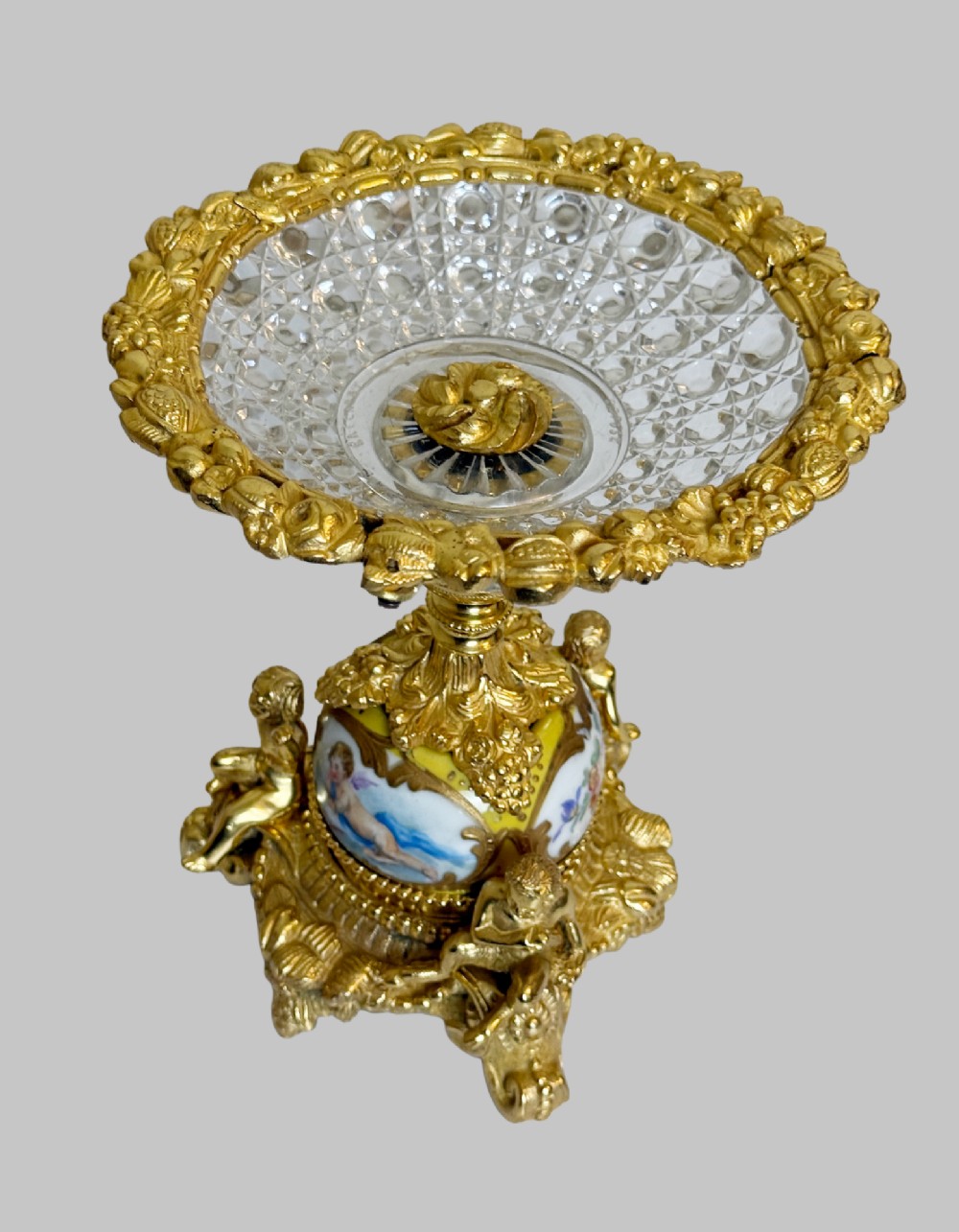 An ornate gilt bronze centrepiece dish featuring a cut crystal bowl, hand-painted porcelain cherub panels, and three seated bronze putti figures on a scrolled base. View III
