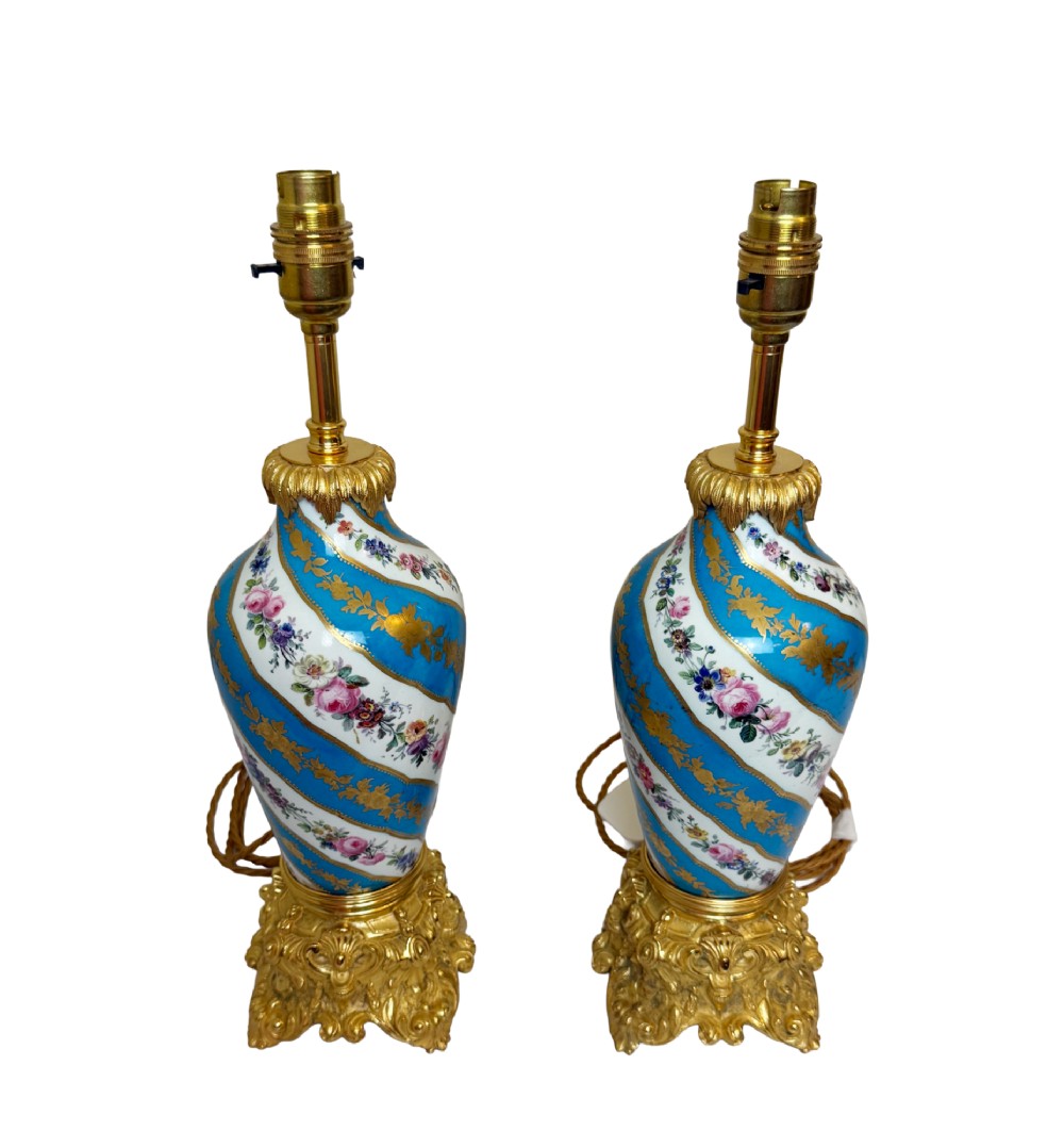 A pair of 19th-century Sevres style table lamps featuring spiral turquoise blue and white porcelain bodies decorated with painted flowers and gold gilding, set on ornate gilt bronze bases.