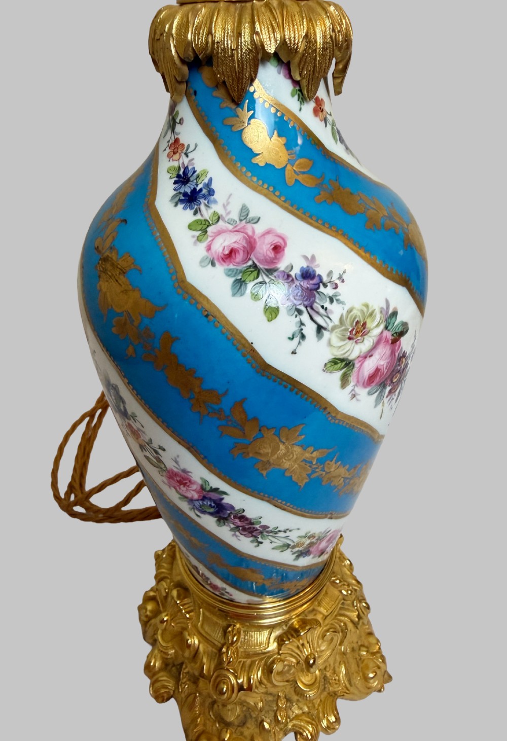 A pair of 19th-century Sevres style table lamps featuring spiral turquoise blue and white porcelain bodies decorated with painted flowers and gold gilding, set on ornate gilt bronze bases. View II