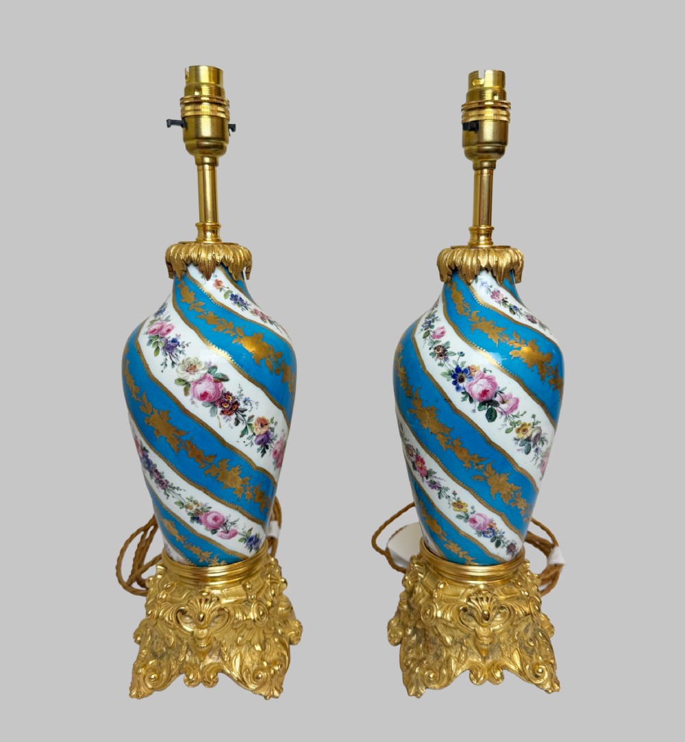 A pair of 19th-century Sevres style table lamps featuring spiral turquoise blue and white porcelain bodies decorated with painted flowers and gold gilding, set on ornate gilt bronze bases. View IV
