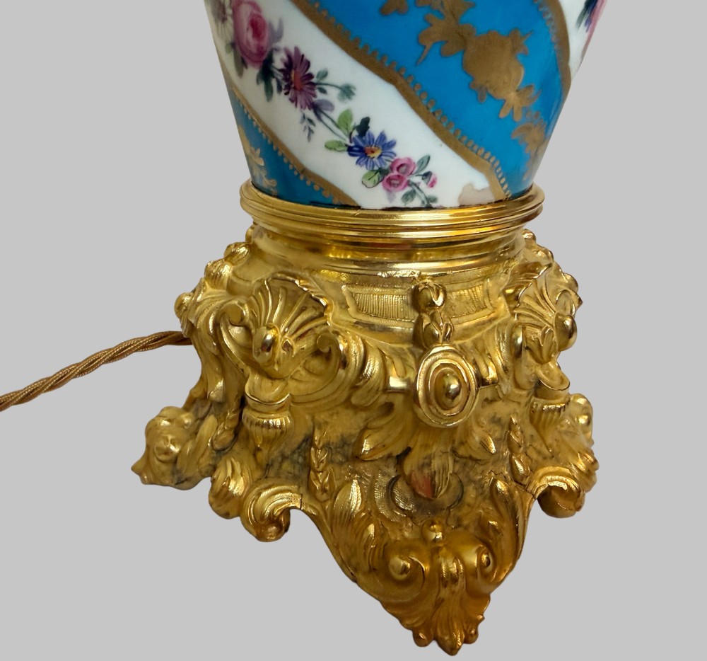 A pair of 19th-century Sevres style table lamps featuring spiral turquoise blue and white porcelain bodies decorated with painted flowers and gold gilding, set on ornate gilt bronze bases. View V