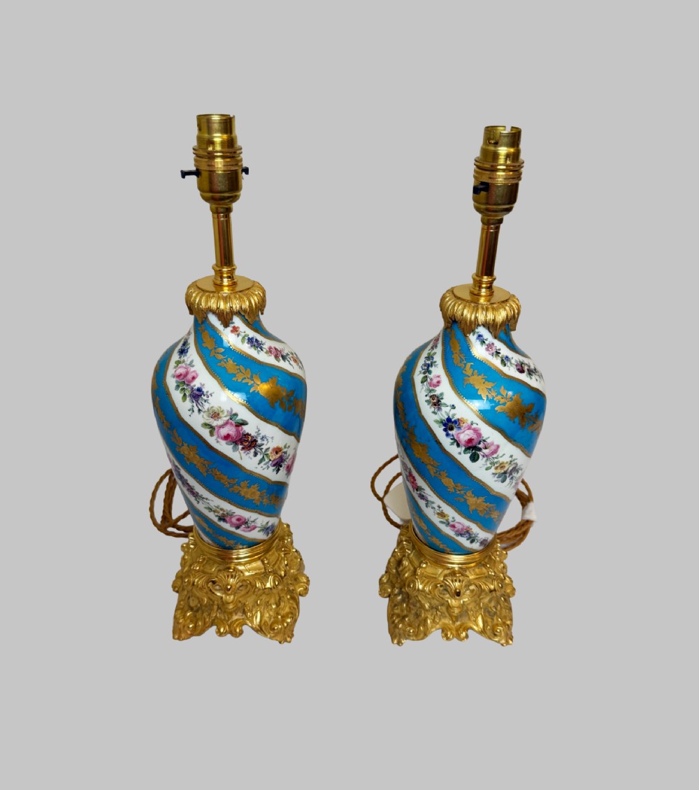 A pair of 19th-century Sevres style table lamps featuring spiral turquoise blue and white porcelain bodies decorated with painted flowers and gold gilding, set on ornate gilt bronze bases. View VII
