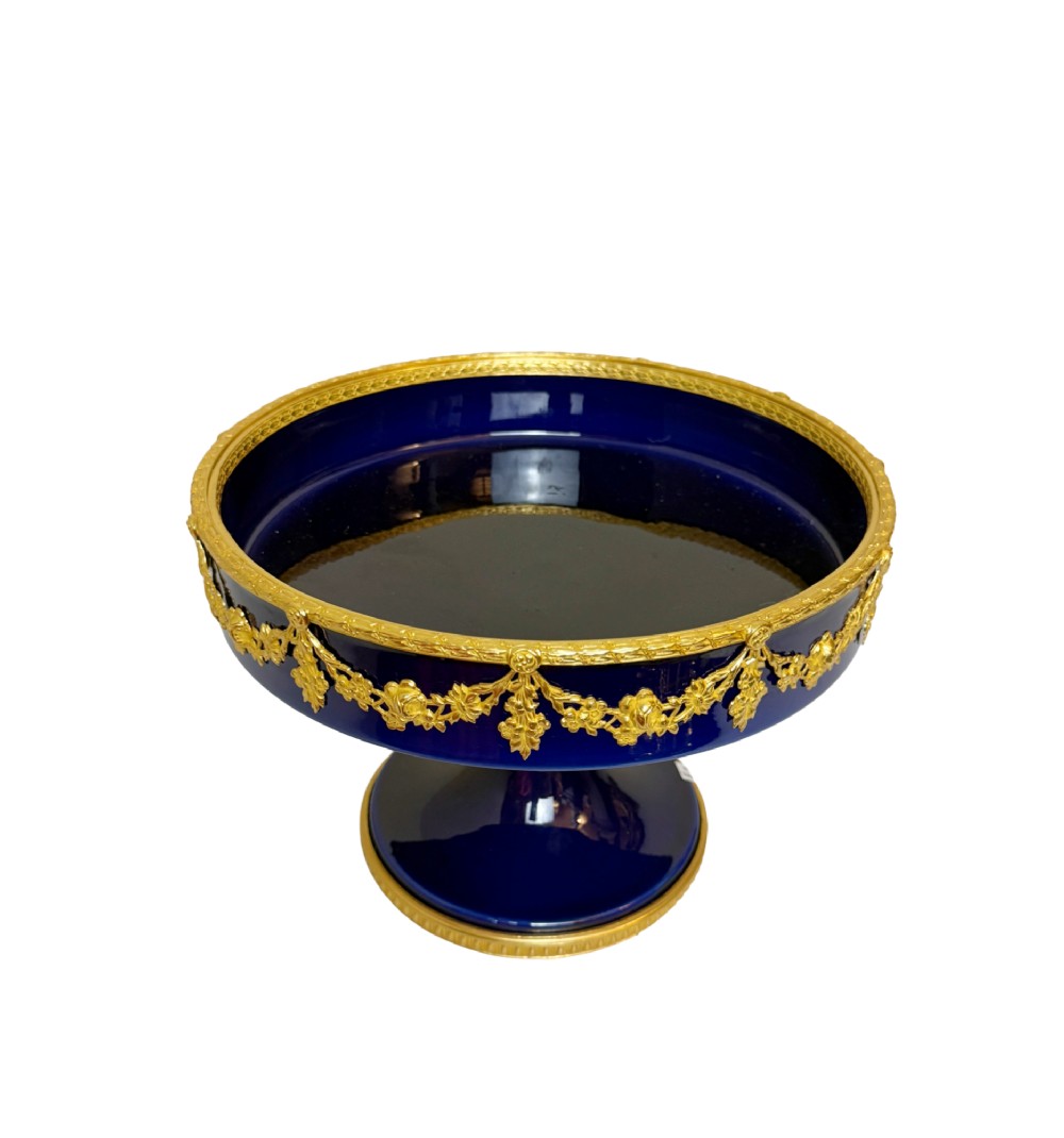 A deep cobalt blue porcelain bowl raised on a pedestal base with ornate gilt bronze floral swags and a chased rim.