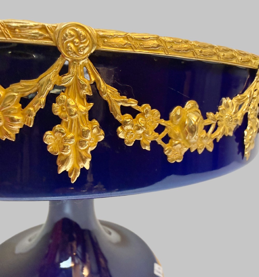 A deep cobalt blue porcelain bowl raised on a pedestal base with ornate gilt bronze floral swags and a chased rim. View VI