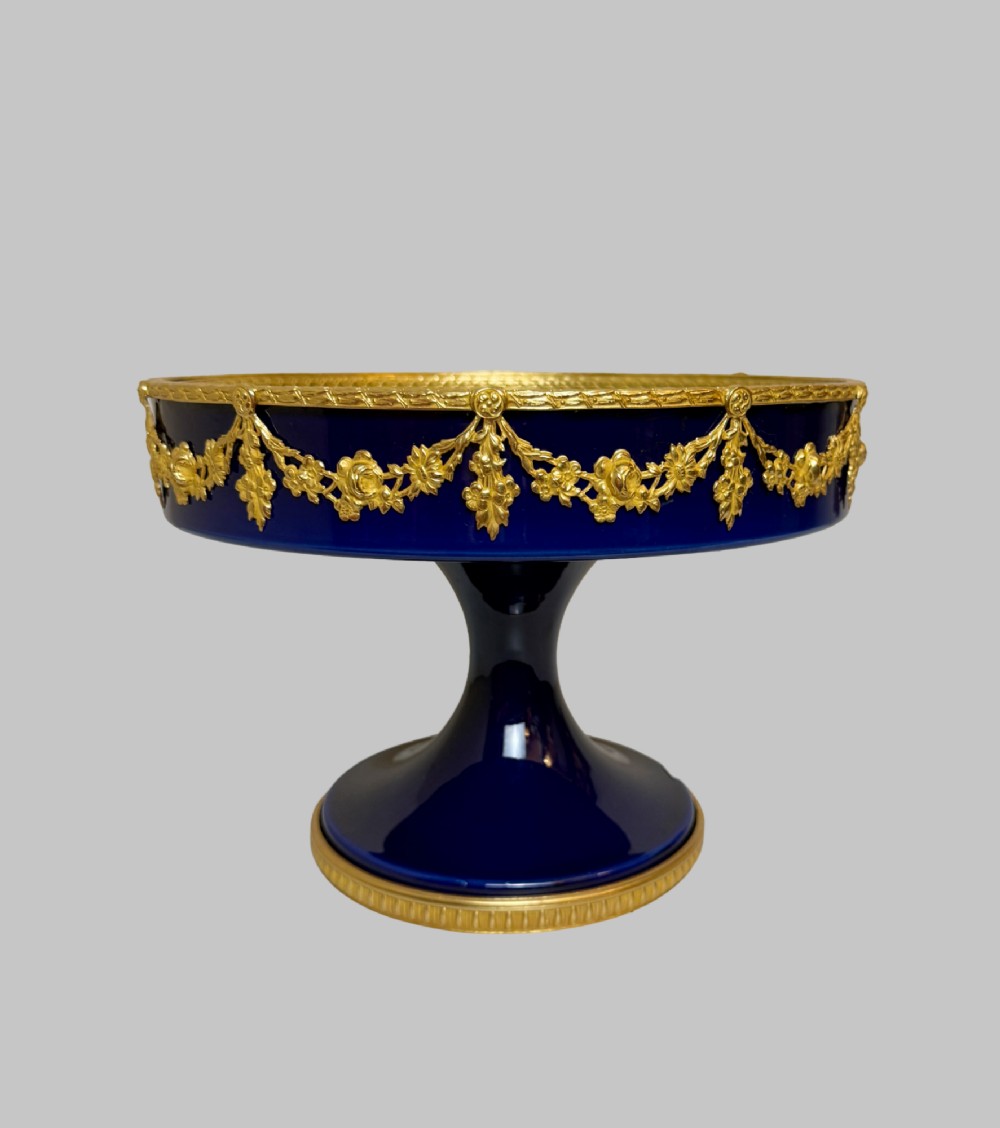 A deep cobalt blue porcelain bowl raised on a pedestal base with ornate gilt bronze floral swags and a chased rim. View VII