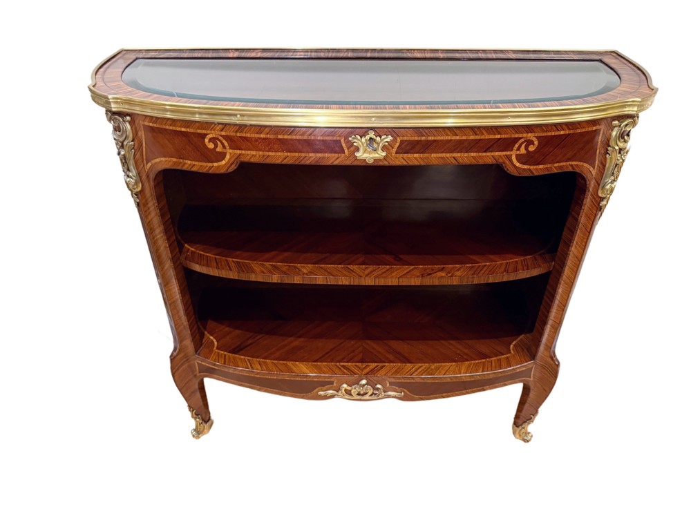 A late 19th-century French Louis XV style demilune open bookcase featuring marquetry wood veneer, gilt-bronze ormolu mounts, open shelving, and a glass vitrine top.