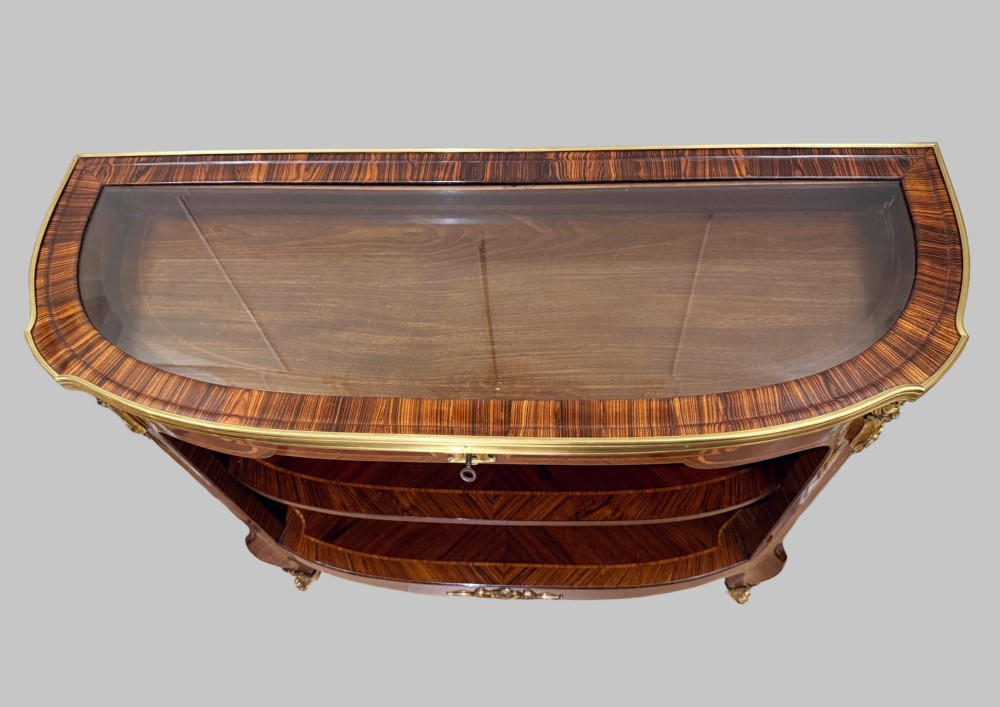A late 19th-century French Louis XV style demilune open bookcase featuring marquetry wood veneer, gilt-bronze ormolu mounts, open shelving, and a glass vitrine top. View II