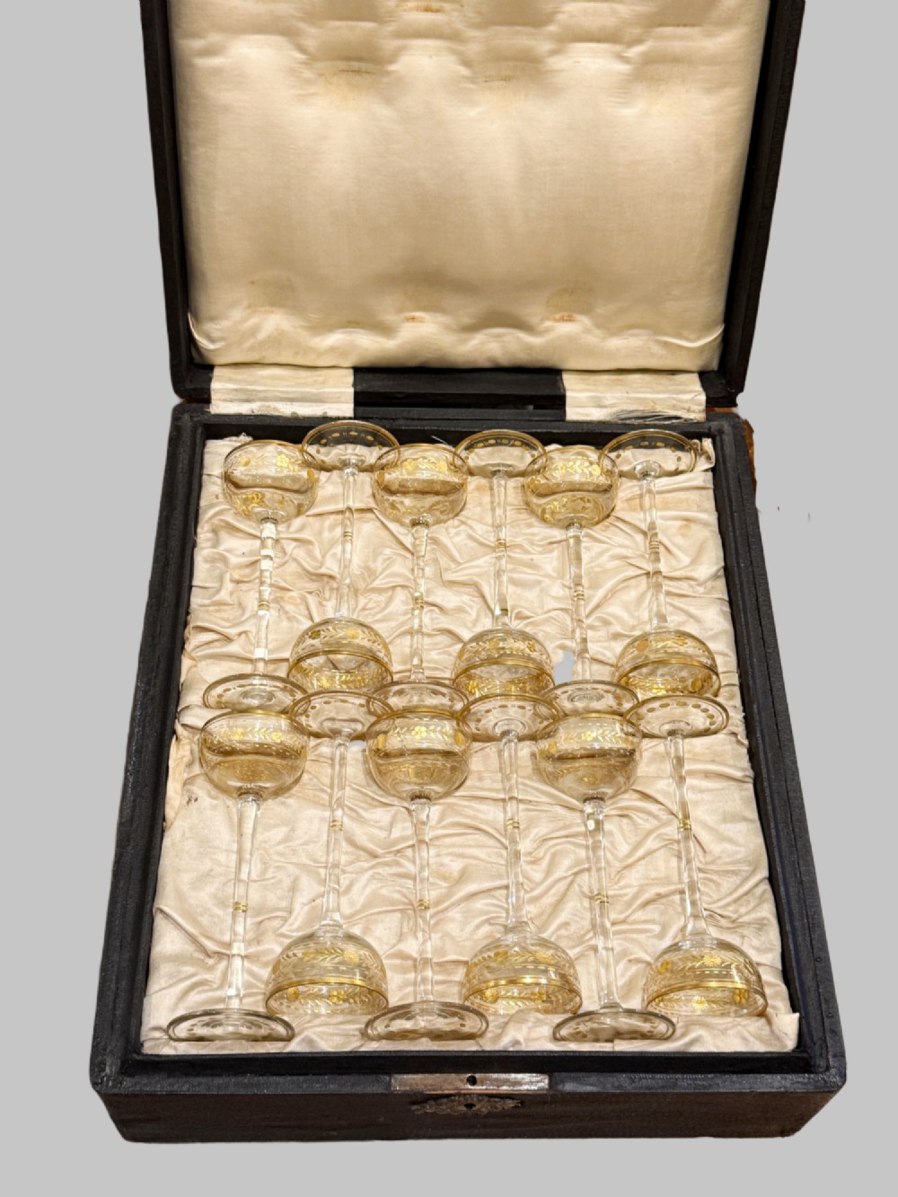 A set of twelve delicate clear glass liqueur stemware pieces with gilt decoration, resting in a padded silk-lined fitted black case. View VI