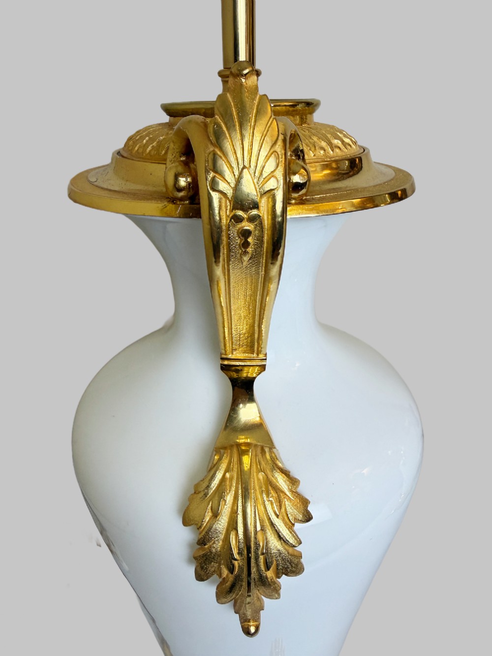 A pair of late nineteenth-century urn-shaped white glass table lamps featuring ornate gilt bronze handles, foliage mounts, and decorative cast bases. View VI