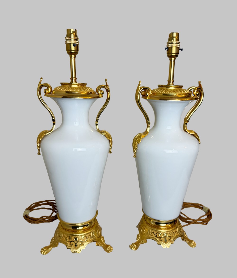 A pair of late nineteenth-century urn-shaped white glass table lamps featuring ornate gilt bronze handles, foliage mounts, and decorative cast bases. View VII