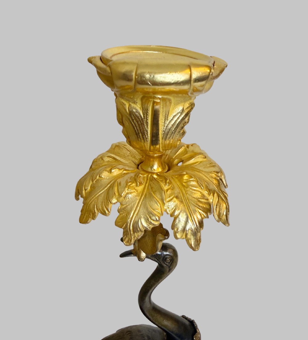 A pair of late nineteenth-century gilt and patinated bronze candlesticks featuring standing birds holding palm stems with floral candle nozzles atop rocky bases. View II
