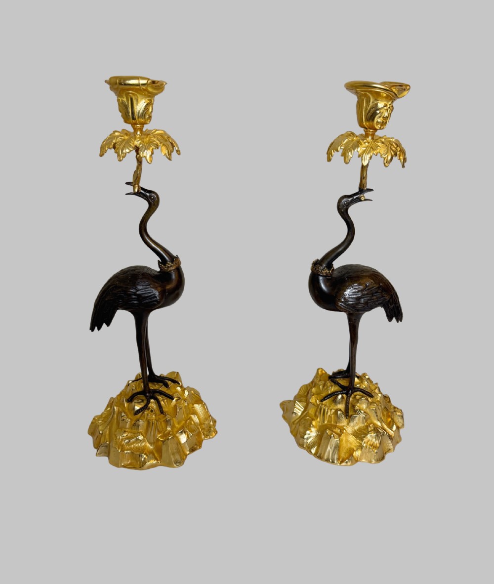 A pair of late nineteenth-century gilt and patinated bronze candlesticks featuring standing birds holding palm stems with floral candle nozzles atop rocky bases. View V