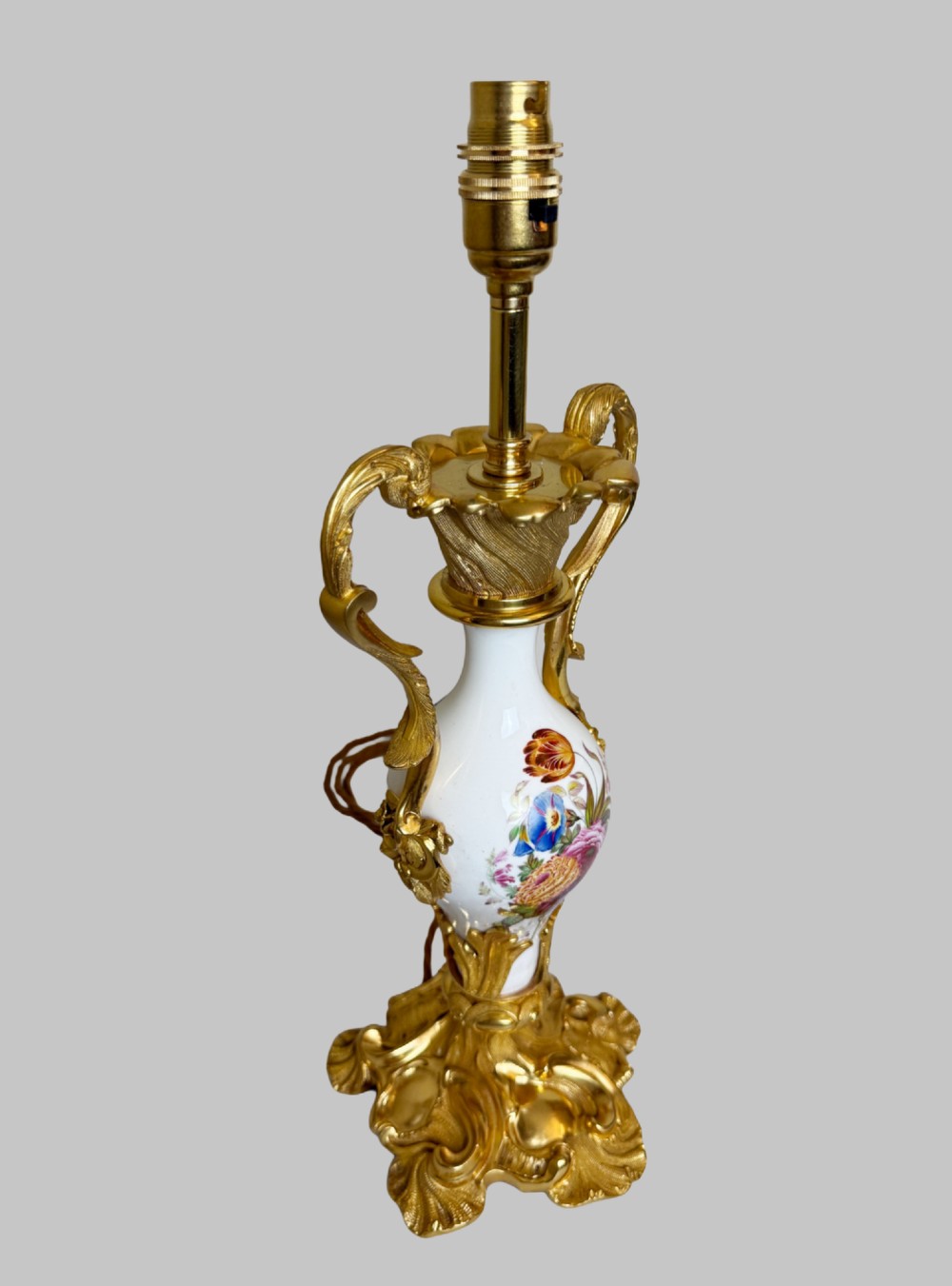 A 19th-century table lamp featuring a white porcelain urn body decorated with hand-painted flowers, set within ornate gilt bronze scroll handles and a rococo leaf base. View II