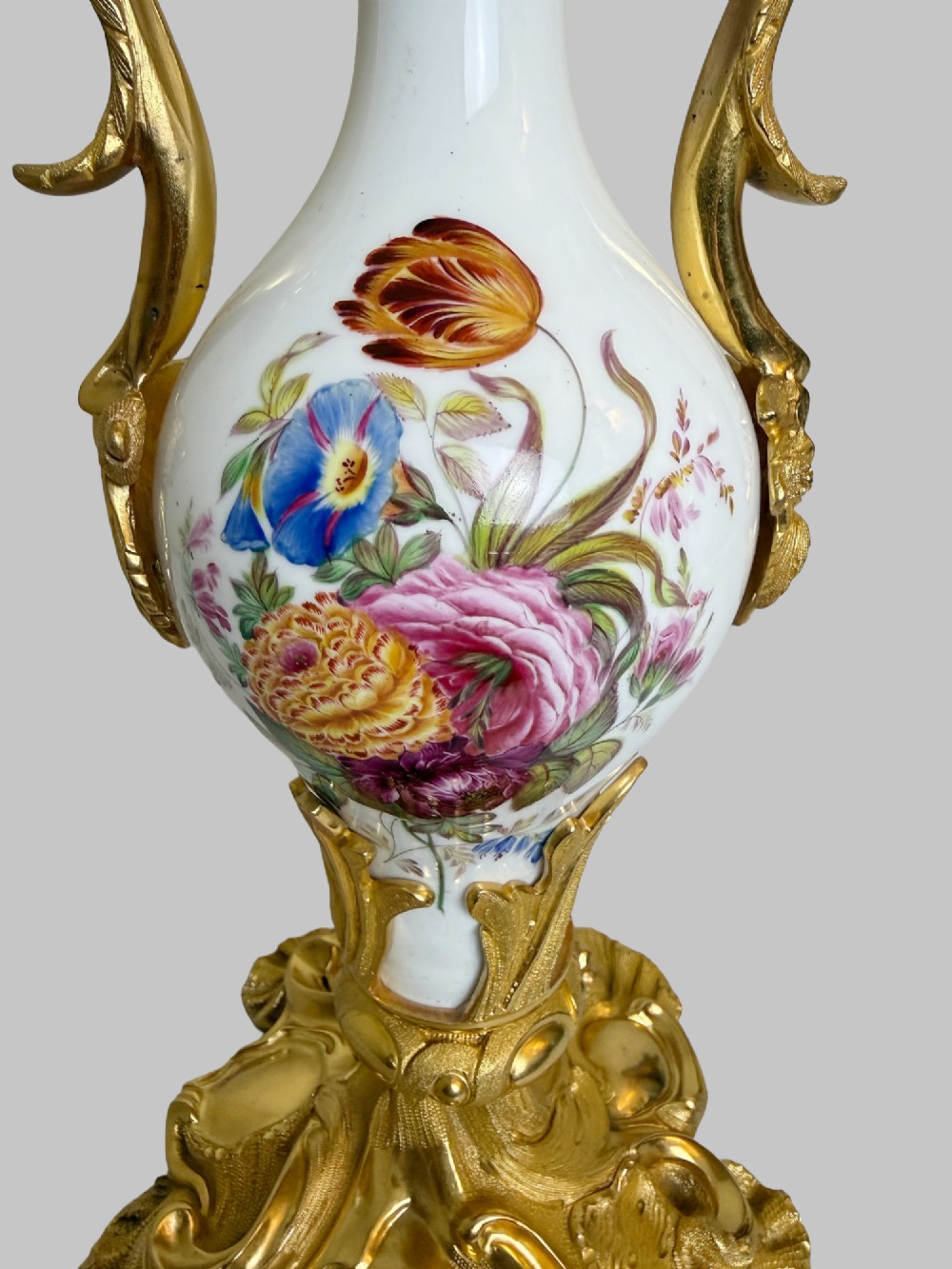 A 19th-century table lamp featuring a white porcelain urn body decorated with hand-painted flowers, set within ornate gilt bronze scroll handles and a rococo leaf base. View V