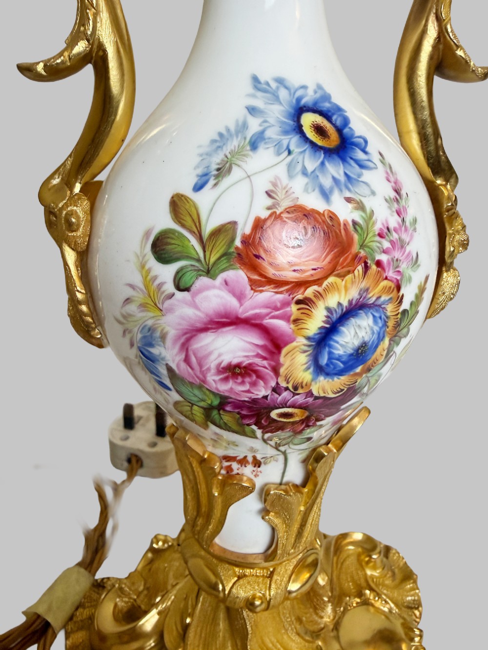 A 19th-century table lamp featuring a white porcelain urn body decorated with hand-painted flowers, set within ornate gilt bronze scroll handles and a rococo leaf base. View VI