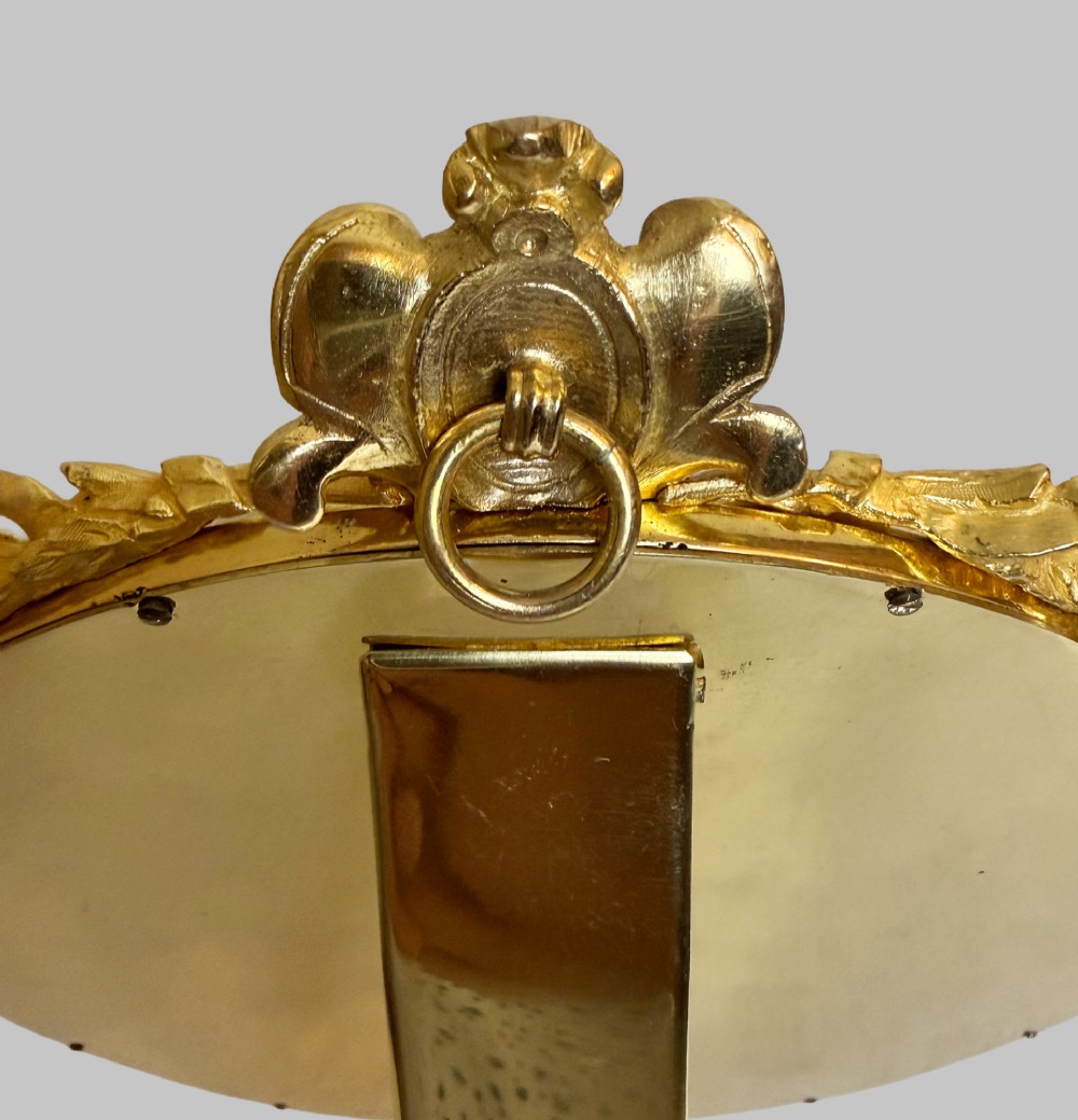 A late 19th-century oval dressing table mirror featuring a gilt bronze frame adorned with blue and purple champleve enamel and bird motifs. View V