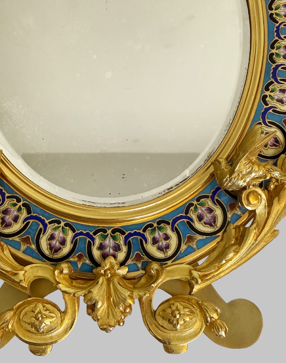 A late 19th-century oval dressing table mirror featuring a gilt bronze frame adorned with blue and purple champleve enamel and bird motifs. View VI