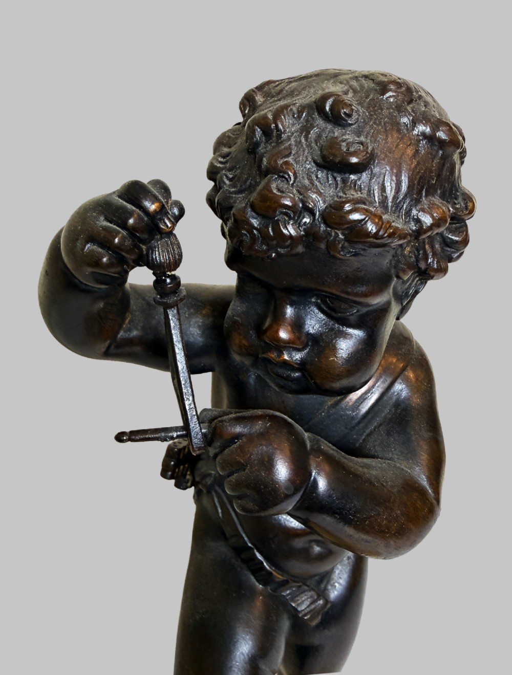 A dark patinated bronze figure of a cherub playing a musical triangle standing on a gilt base mounted on a circular dark wooden plinth. View III