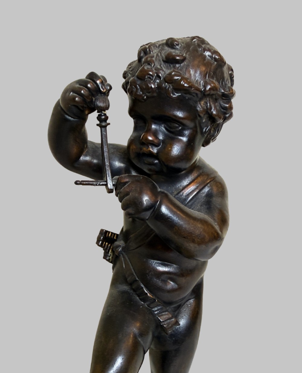 A dark patinated bronze figure of a cherub playing a musical triangle standing on a gilt base mounted on a circular dark wooden plinth. View VII