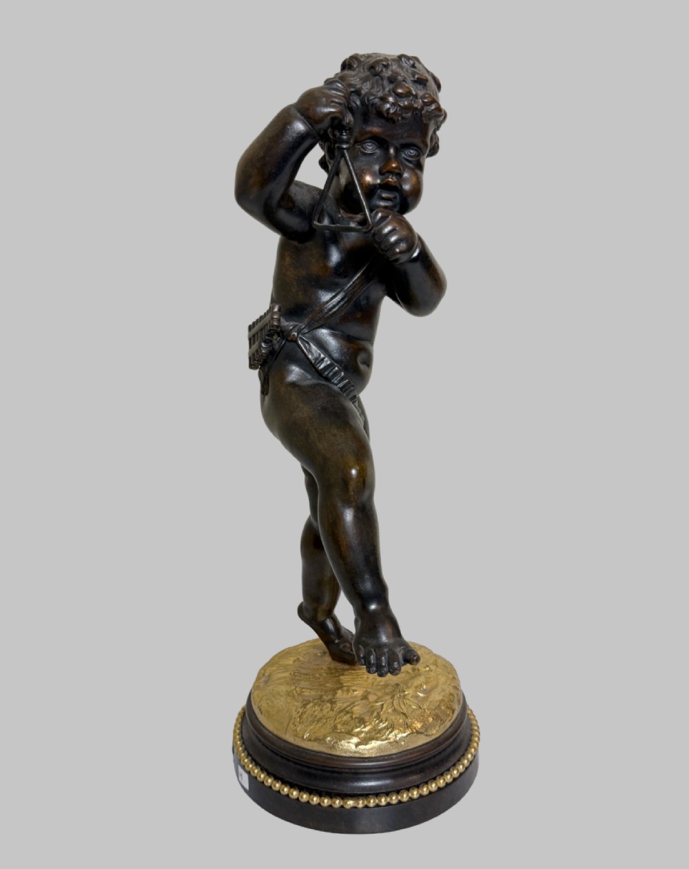 A dark patinated bronze figure of a cherub playing a musical triangle standing on a gilt base mounted on a circular dark wooden plinth. View VIII