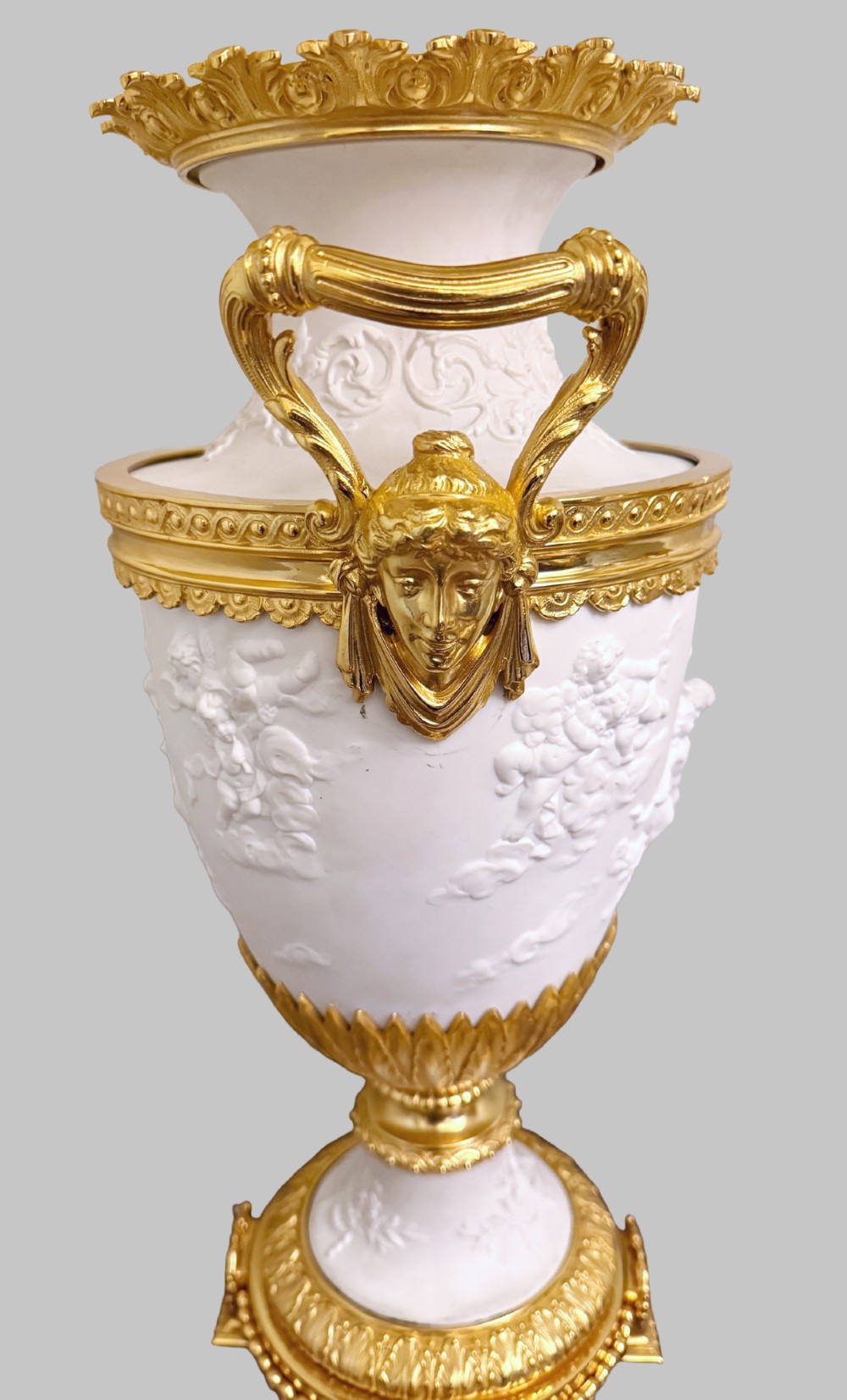 A pair of white porcelain urns adorned with raised relief putti motifs and detailed gilt bronze bases, handles, and rims. View III