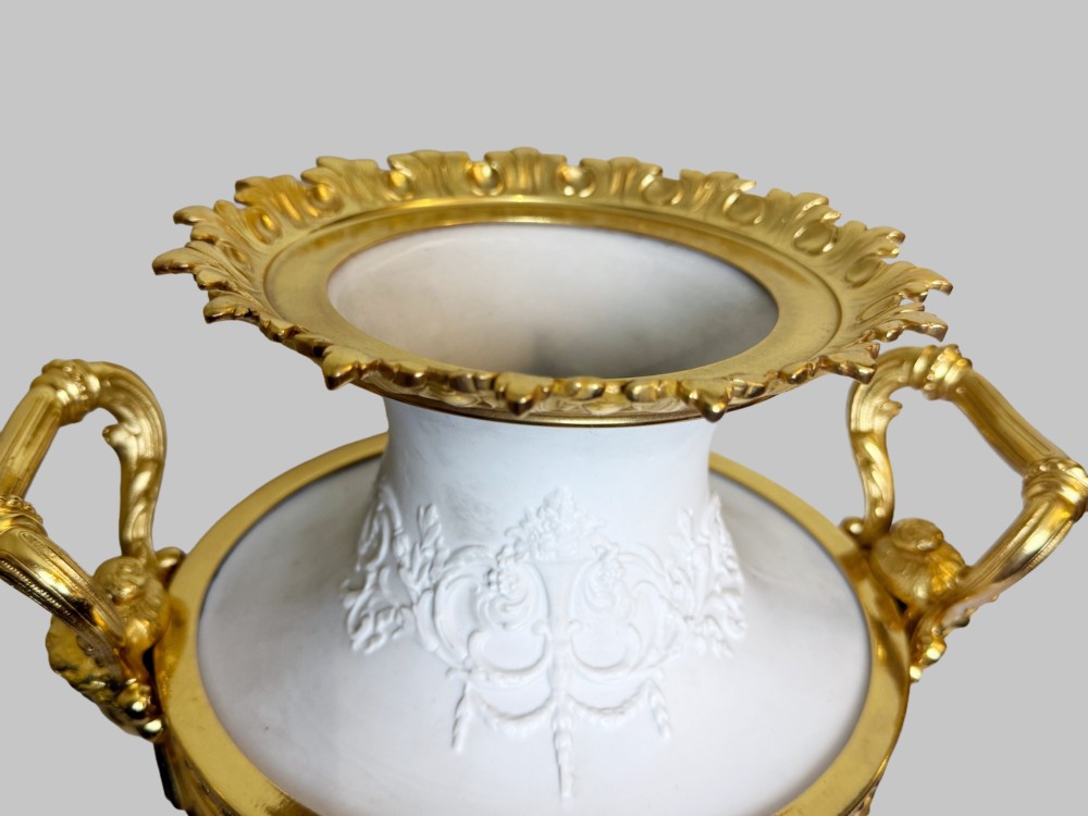 A pair of white porcelain urns adorned with raised relief putti motifs and detailed gilt bronze bases, handles, and rims. View V