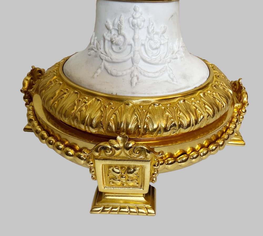 A pair of white porcelain urns adorned with raised relief putti motifs and detailed gilt bronze bases, handles, and rims. View VIII