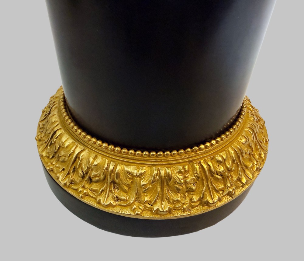 A pair of late 19th-century patinated and gilt bronze urn coupes set upon black marble pedestal bases with detailed leaf motifs. View II