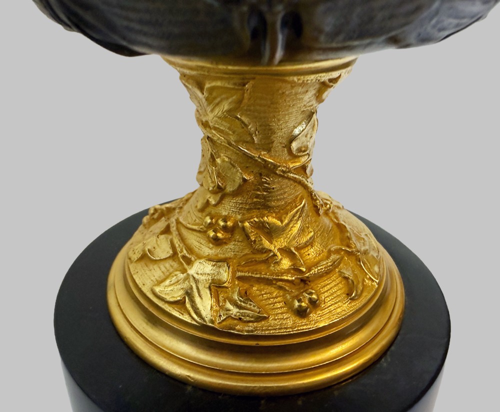A pair of late 19th-century patinated and gilt bronze urn coupes set upon black marble pedestal bases with detailed leaf motifs. View V
