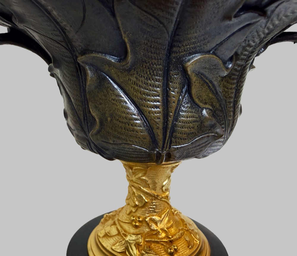 A pair of late 19th-century patinated and gilt bronze urn coupes set upon black marble pedestal bases with detailed leaf motifs. View VI