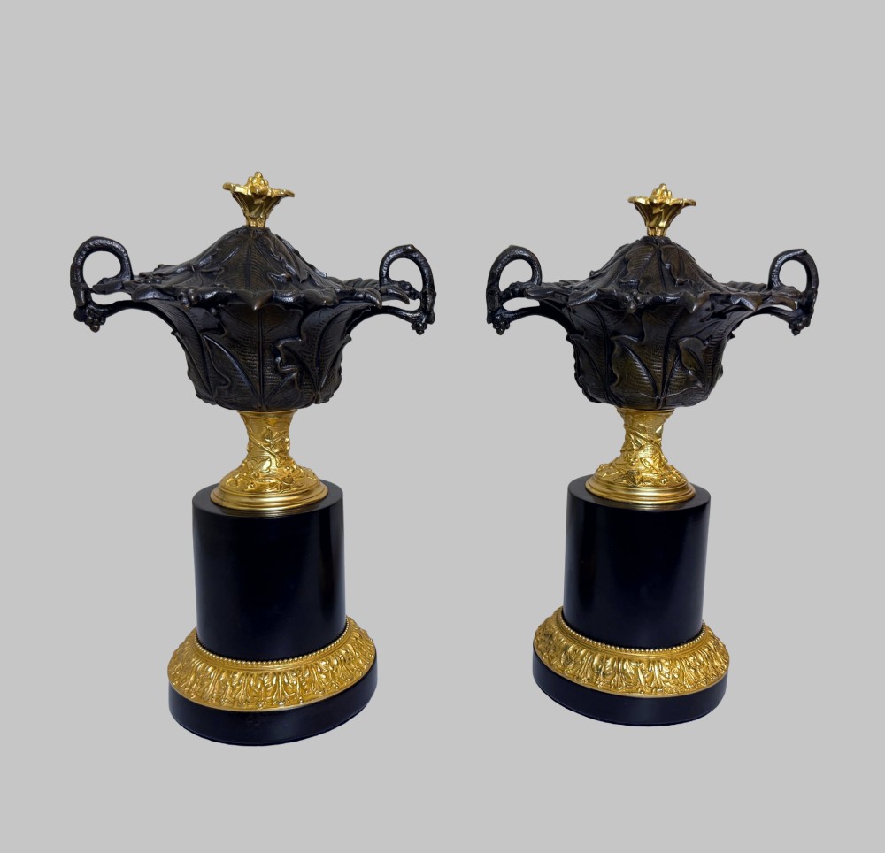 A pair of late 19th-century patinated and gilt bronze urn coupes set upon black marble pedestal bases with detailed leaf motifs. View VIII