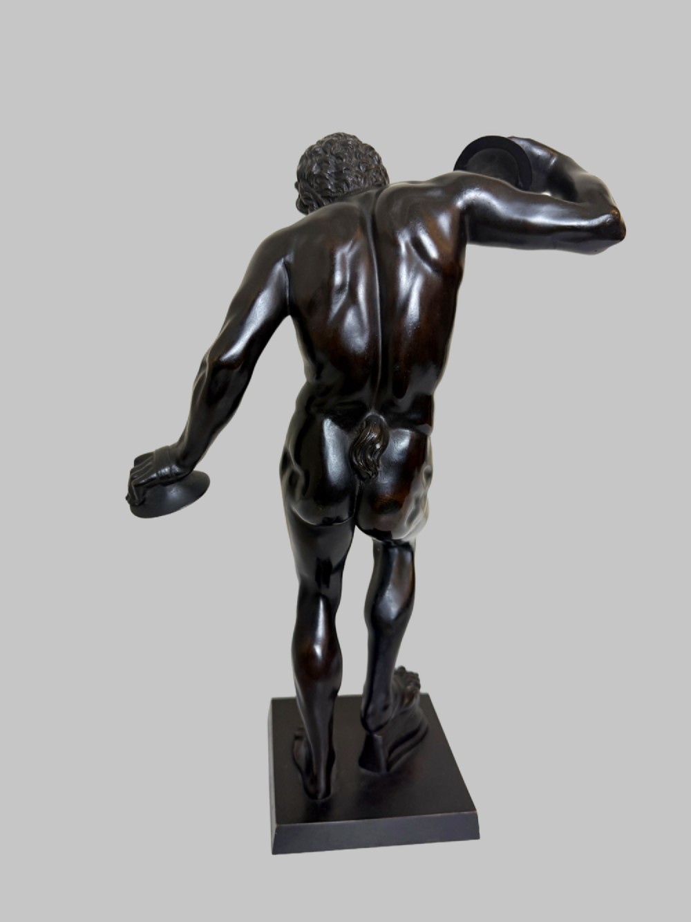 A dark patinated bronze statue depicting a nude classical dancing faun holding cymbals, mounted on a square black base. View III
